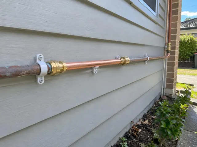 Repaired copper water pipe fixed to weatherboard wall beside brick corner in Caringbah