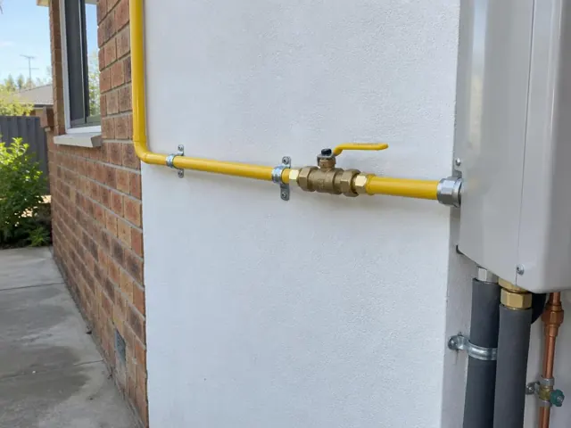 Yellow gas pipe and valve mounted on an exterior brick and rendered wall in Sylvania