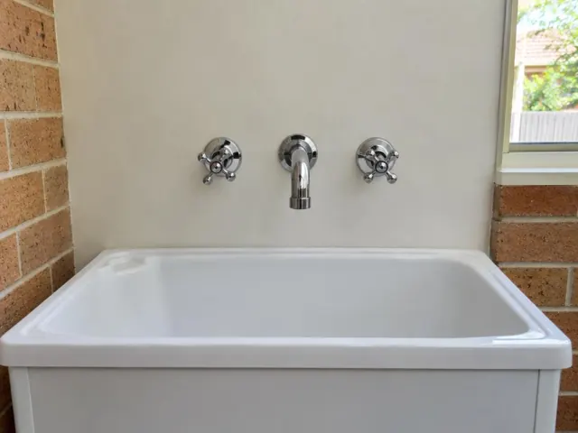 White laundry sink with chrome taps and spout against a light wall and brick side walls in Sylvania
